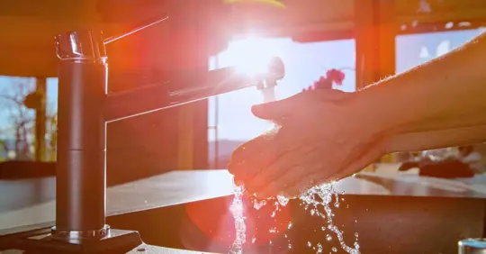 person at washing hands in kitchen sink against harsh sun rays